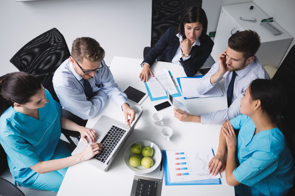 Equipo de salud y recursos humanos trabajando con sistemas digitales de gestión, análisis de datos y cumplimiento normativo en una oficina moderna con tecnología médica avanzada.